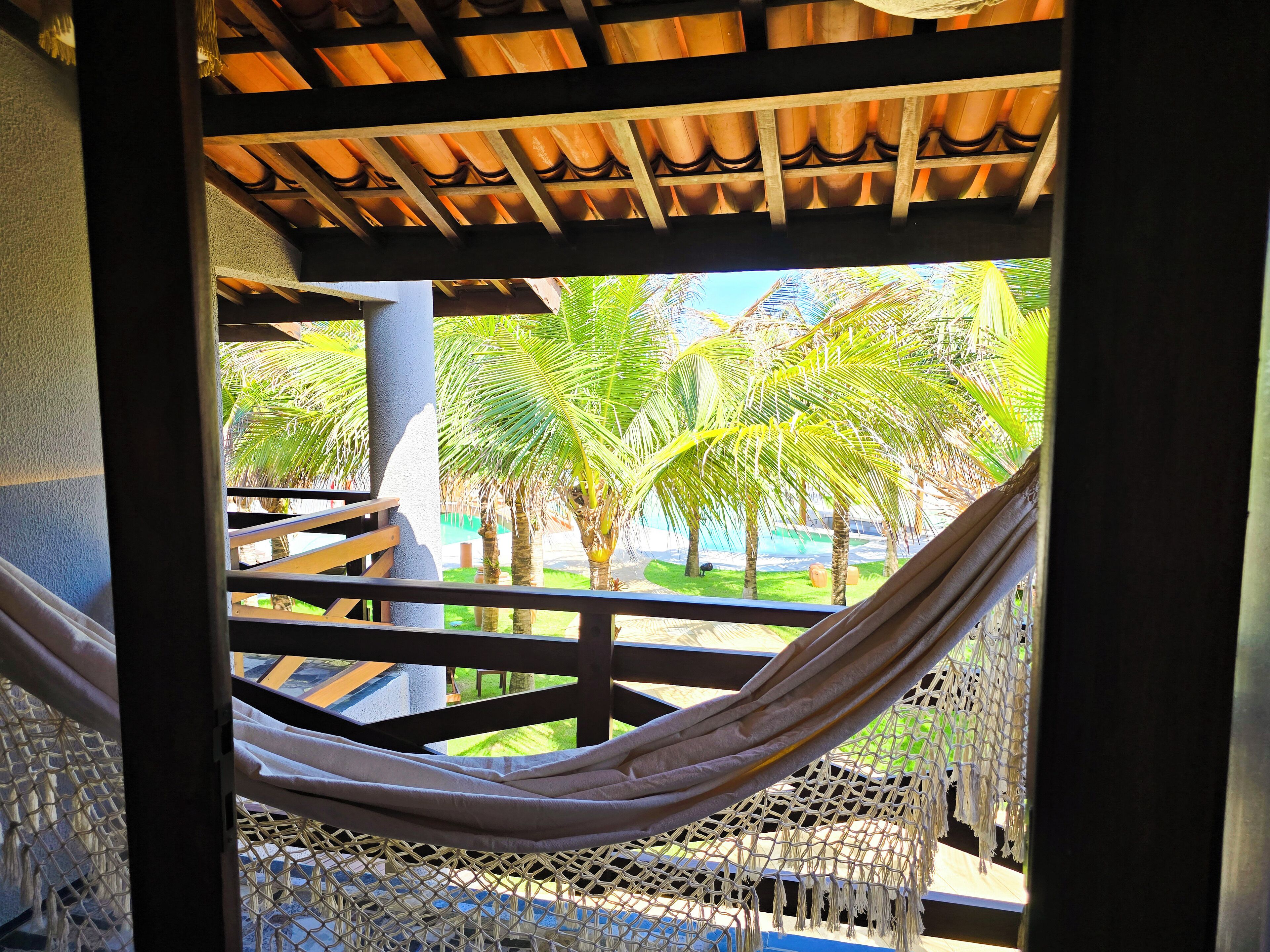 A hammock under a wooden structure with a view of palm trees and a pool.