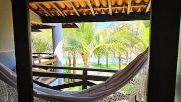 A hammock under a wooden structure with a view of palm trees and a pool.