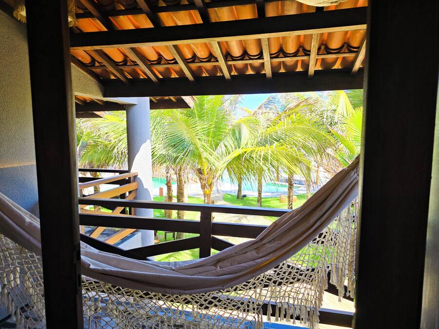 A hammock under a wooden structure with a view of palm trees and a pool.