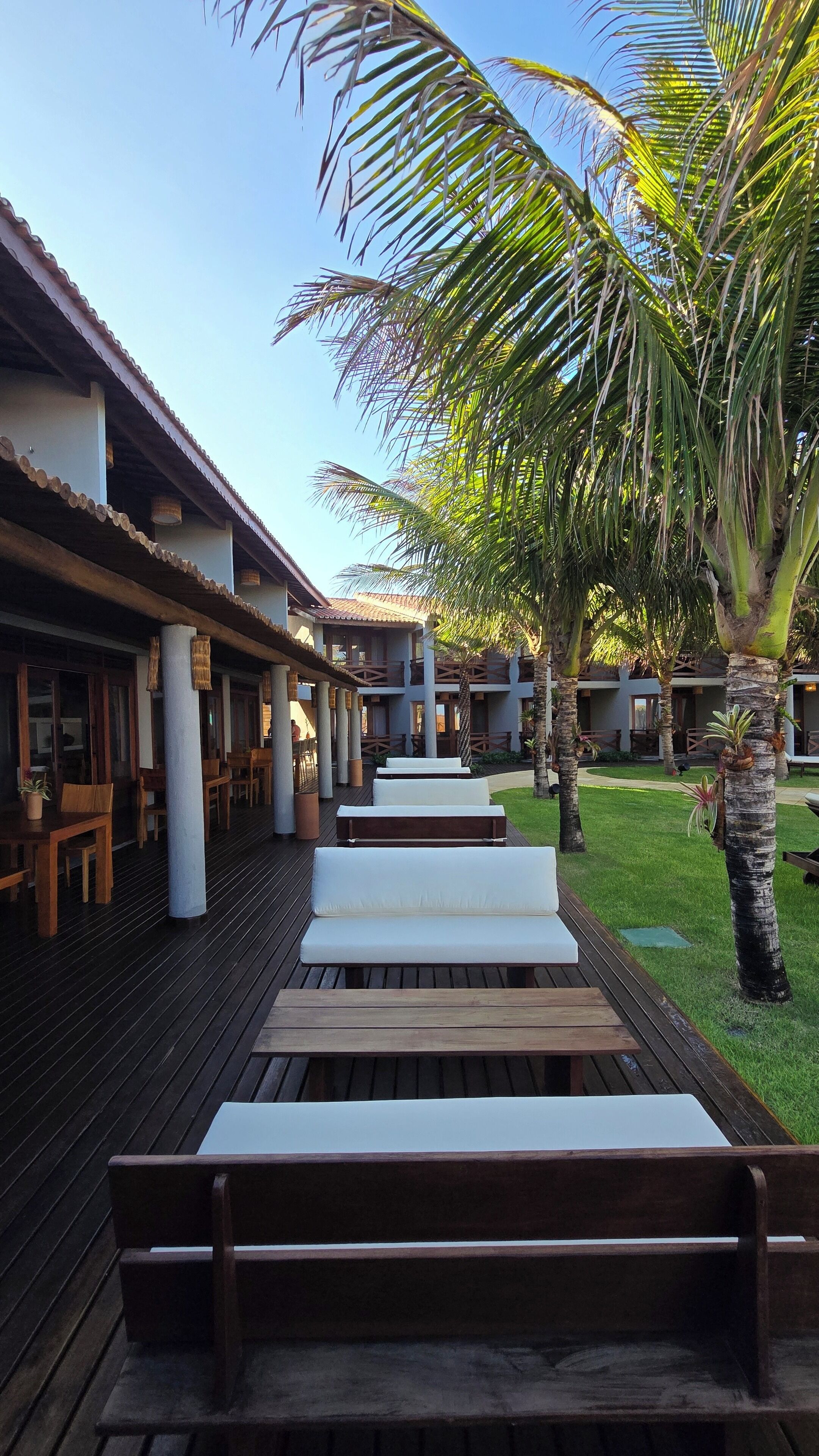 A resort with outdoor seating areas, palm trees, and a building with a tiled roof.