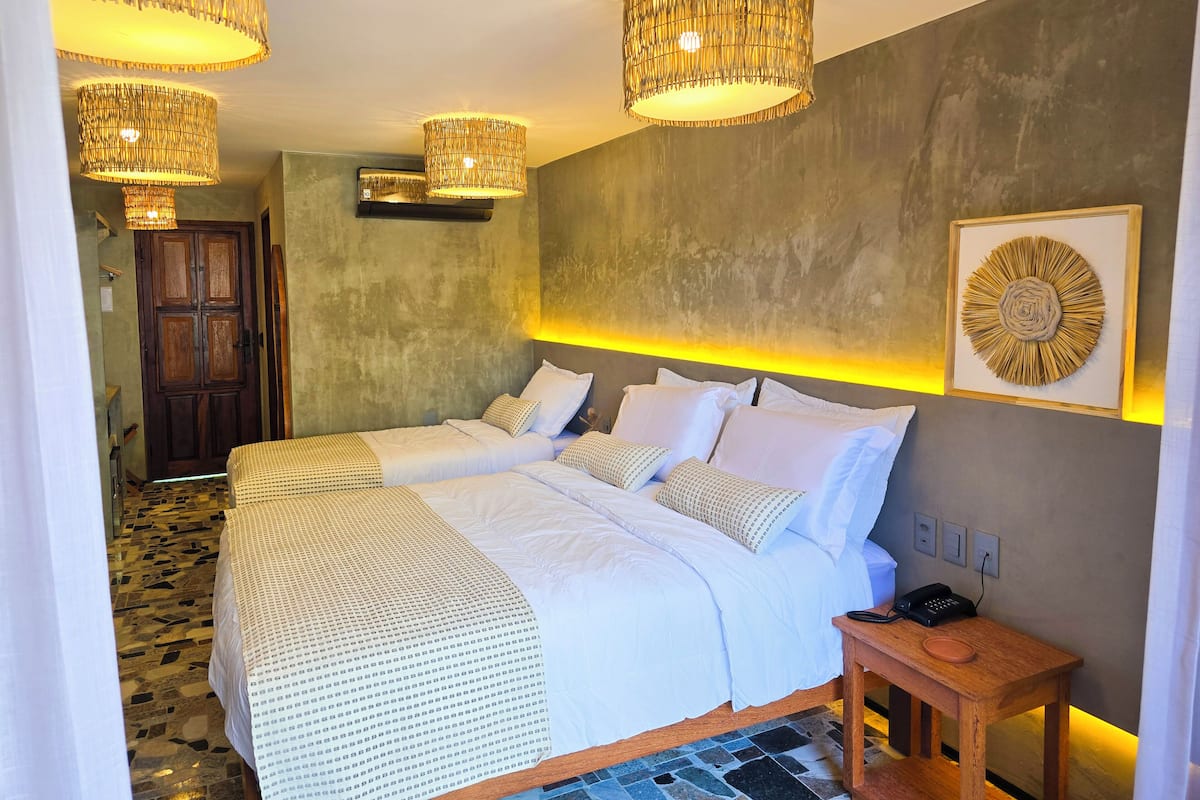 A hotel room with two beds, a wooden nightstand, a wall-mounted light fixture, and a framed artwork.