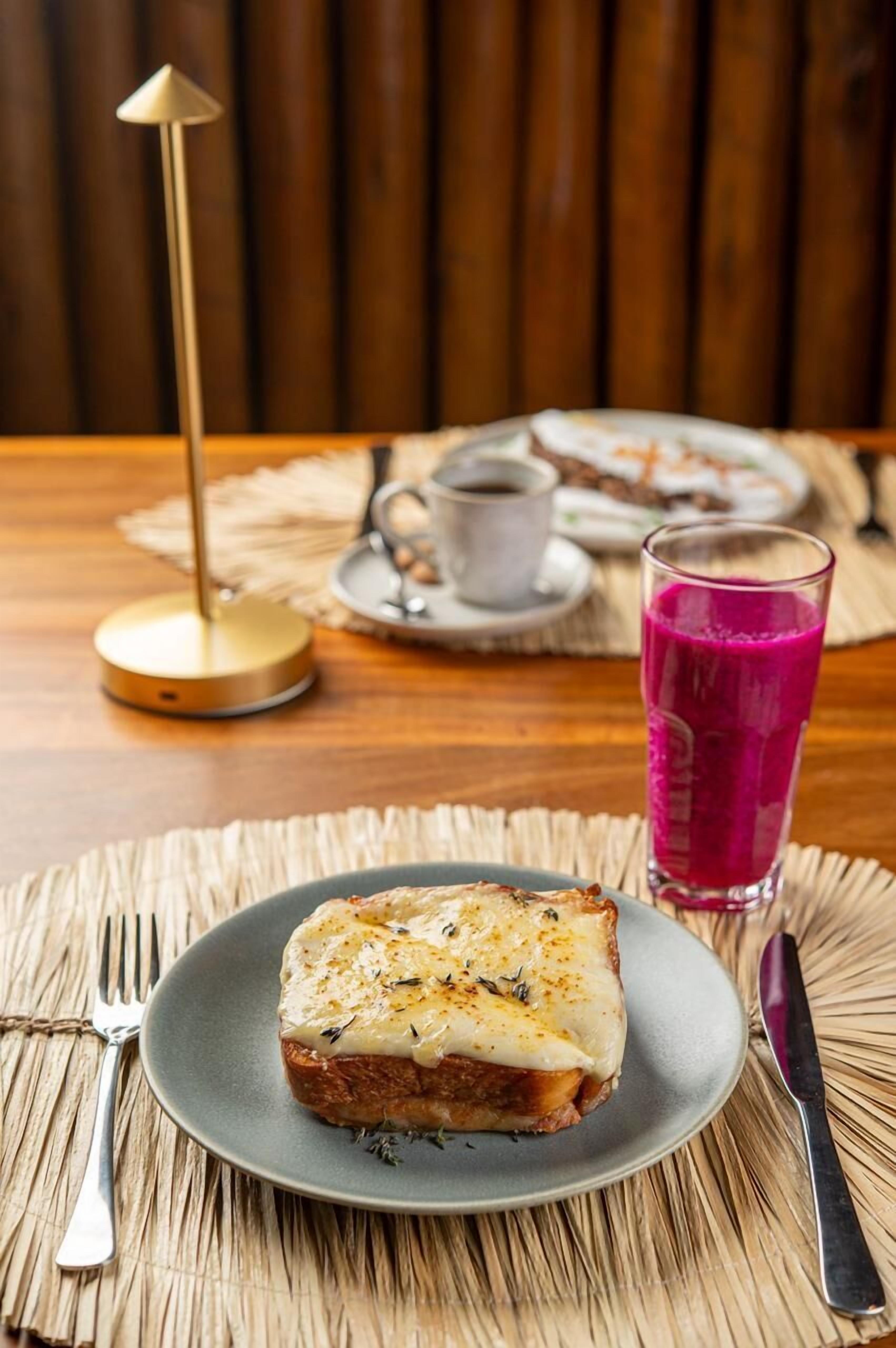 A breakfast setting with a plate of toast, a glass of beetroot juice, and a cup of coffee on a wooden table.