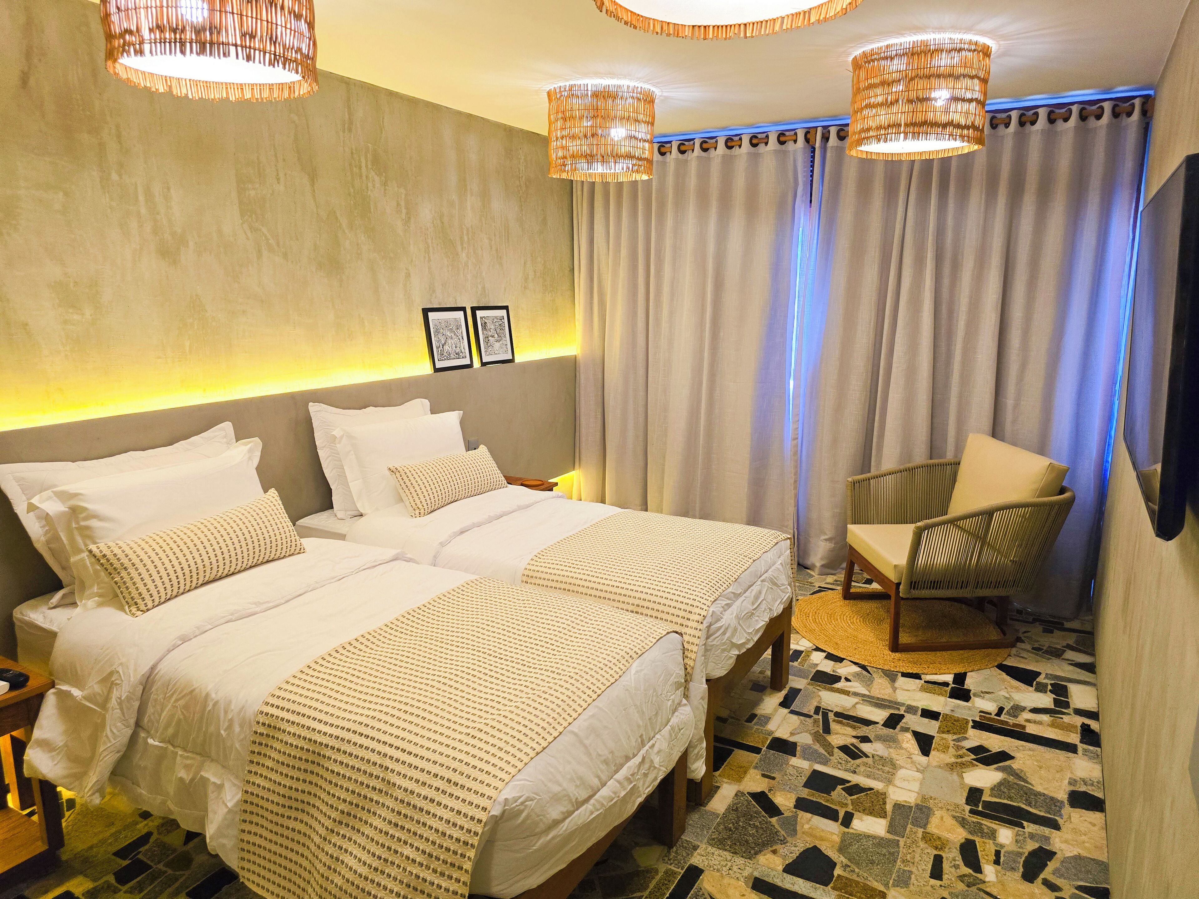 Habitación de hotel con dos camas, una silla, un televisor y piso con diseño.