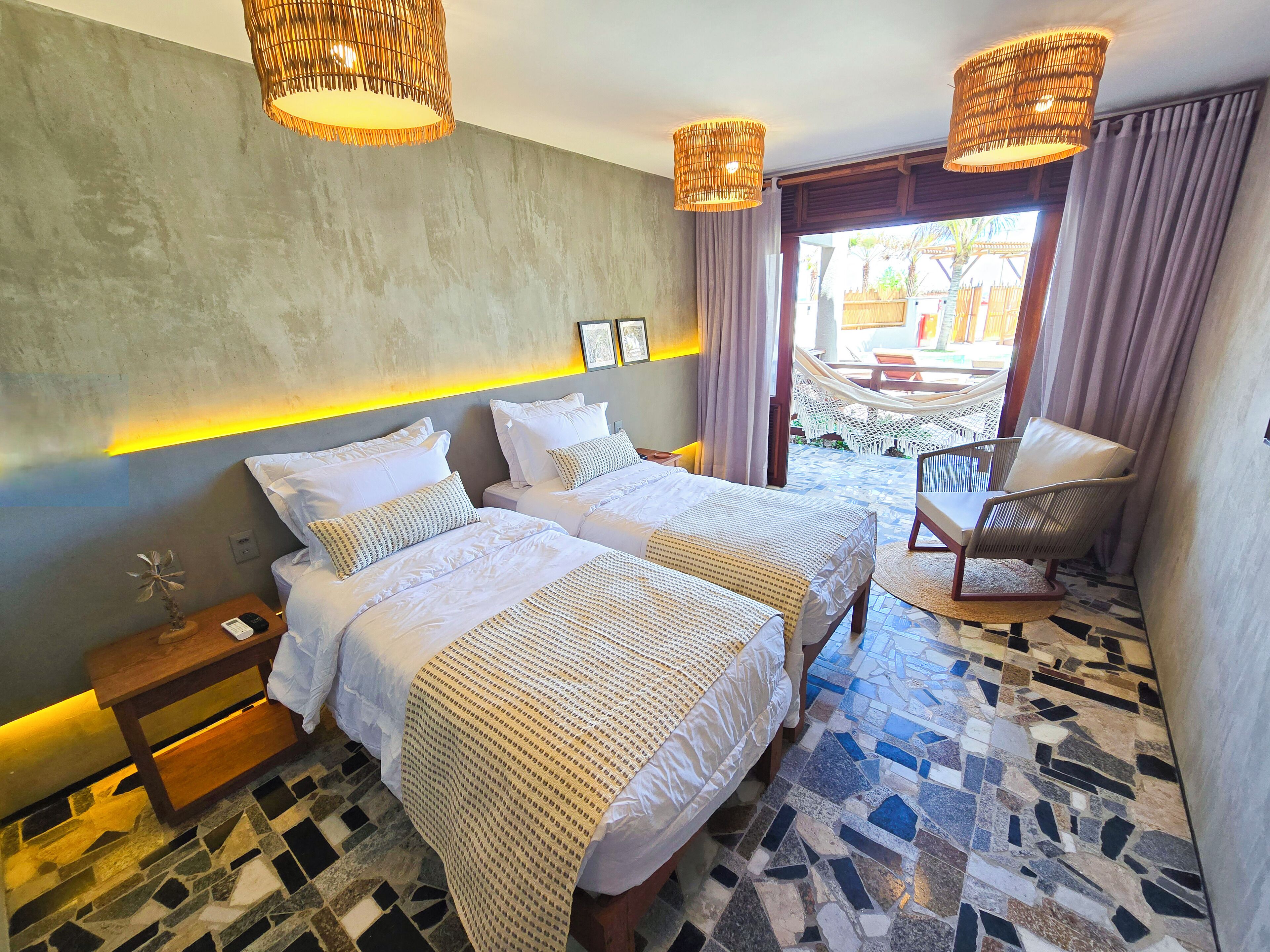 Habitación de hotel con dos camas, una mesita, una silla y vistas al exterior.