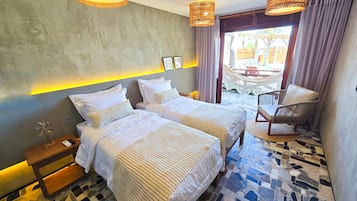 Habitación de hotel con dos camas, una mesita, una silla y vistas al exterior.