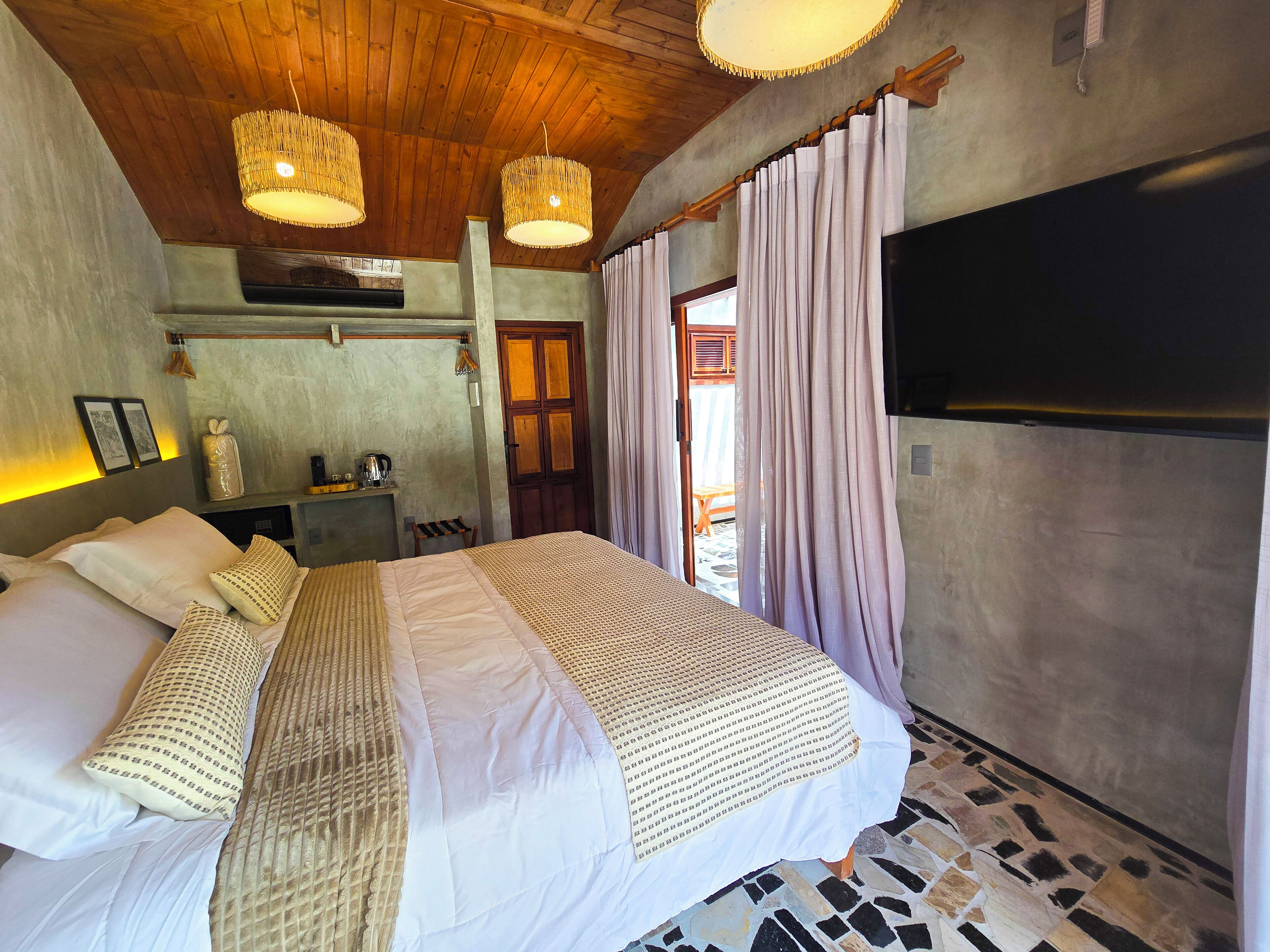 Une chambre avec un grand lit, un plafond en bois et un téléviseur à écran plat fixé au mur.