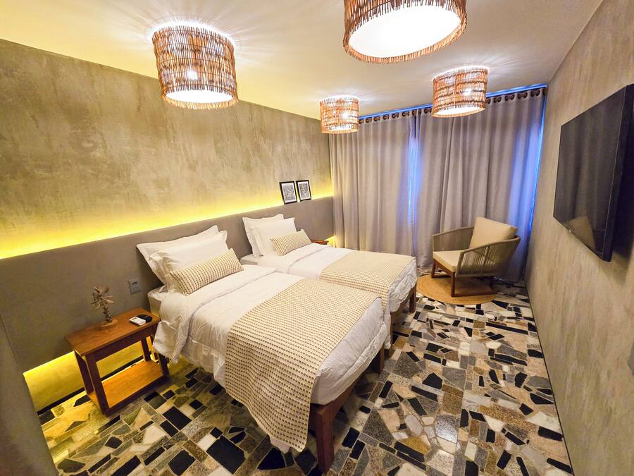 Una habitación de hotel moderna con una cama grande, dos mesitas de noche, una silla, un televisor y un suelo con estampado.