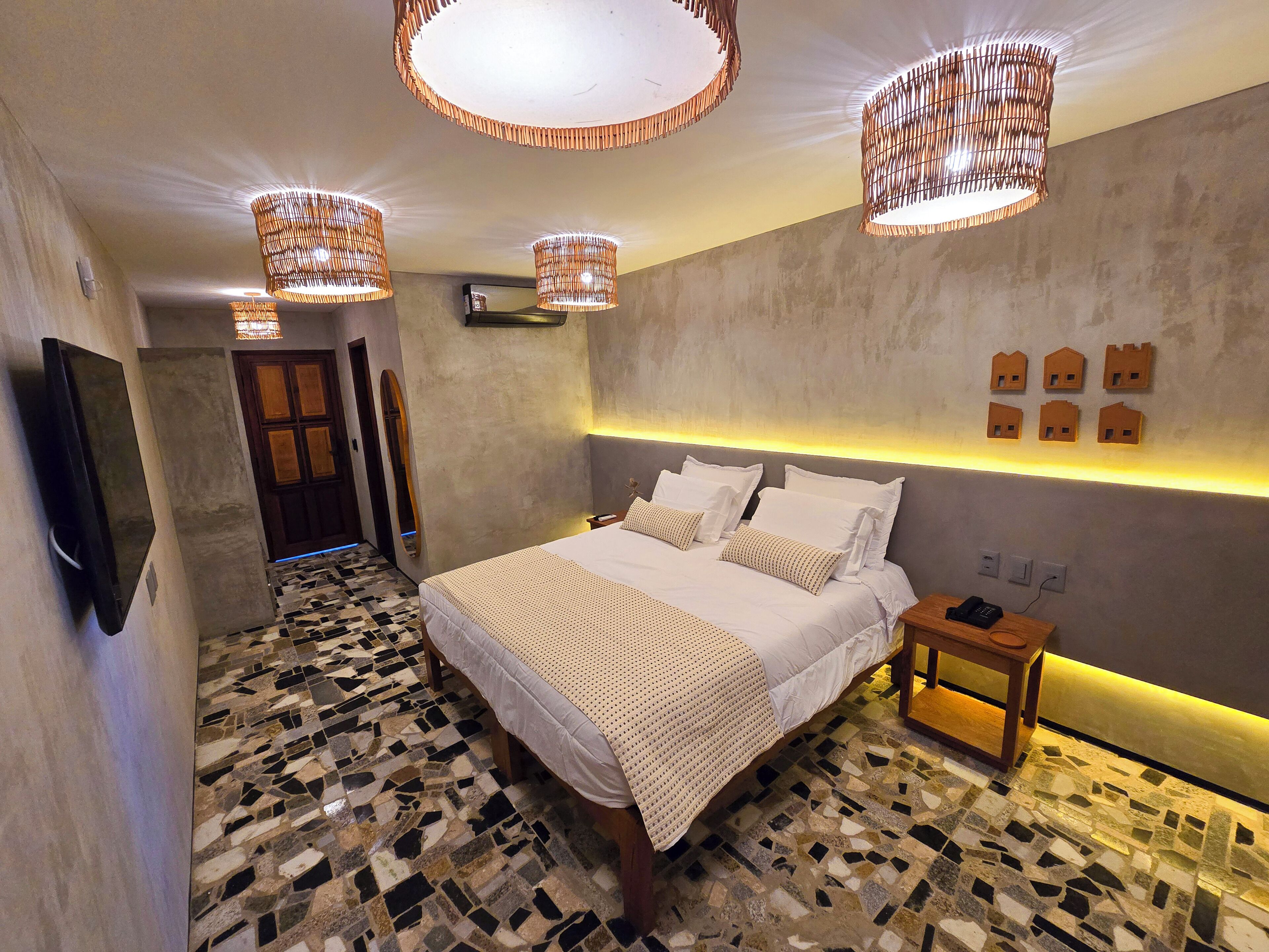 Een moderne slaapkamer met een groot bed, een nachtkastje, een aan de muur bevestigde televisie en een bijzondere plafondlamp.
