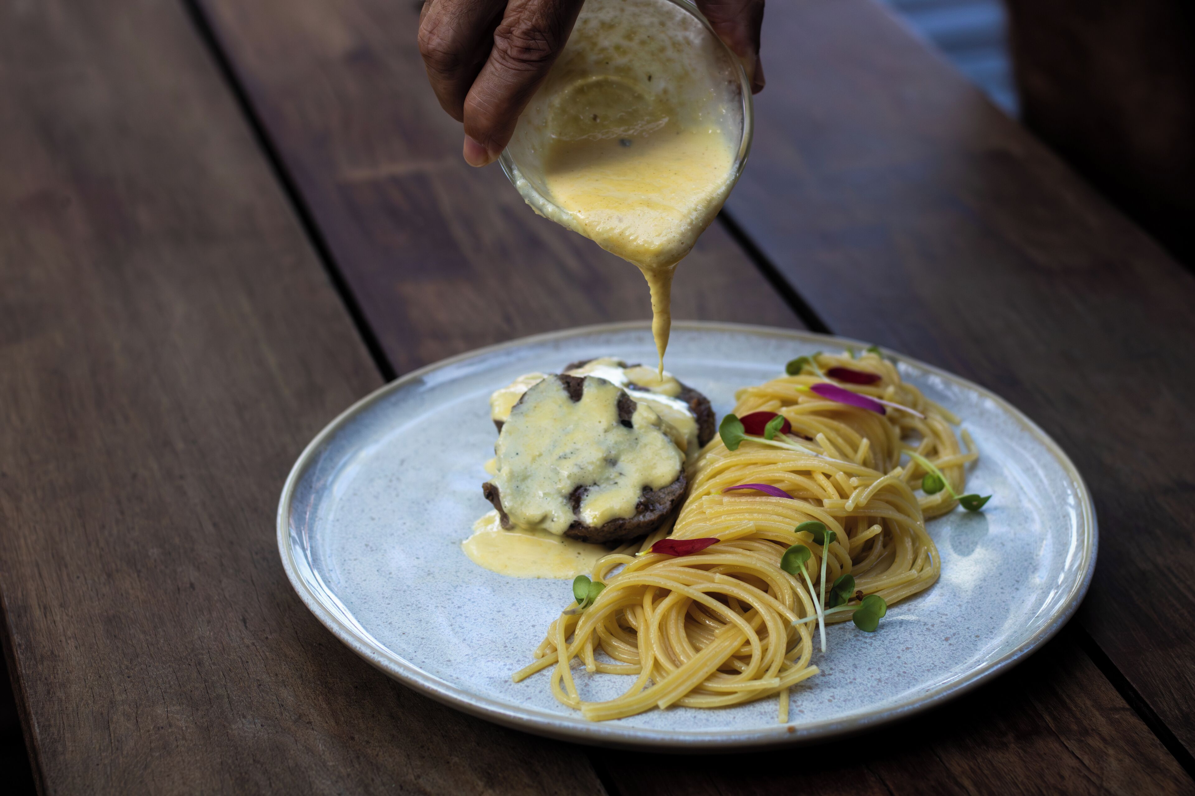 A plate of spaghetti with a meat topping and sauce being poured over it.