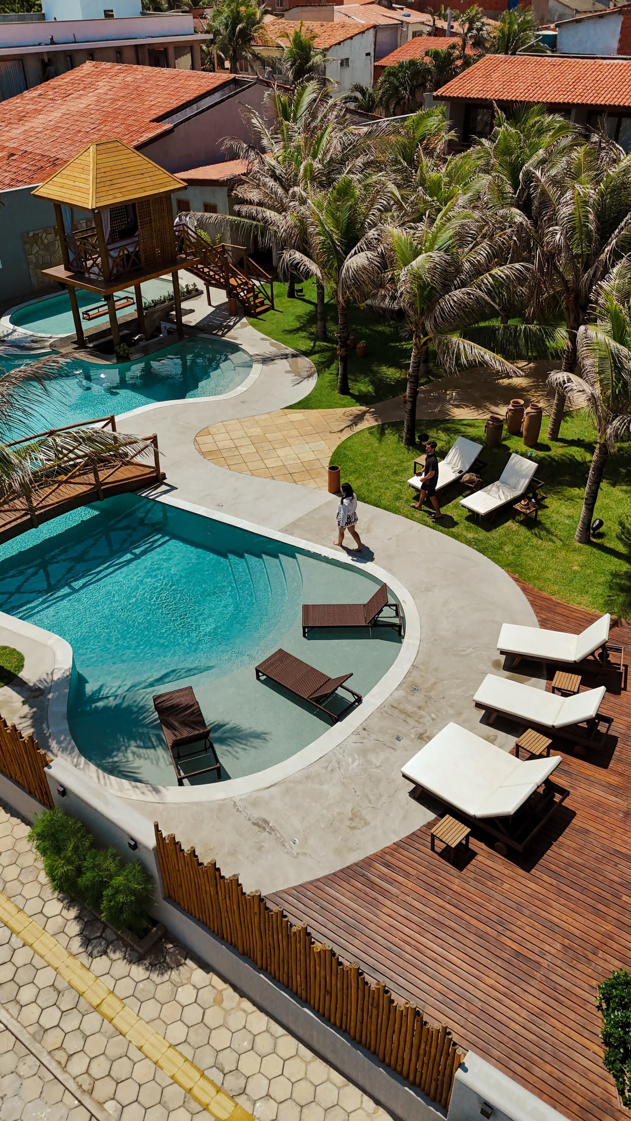 A resort with a large pool, sun loungers, and palm trees.