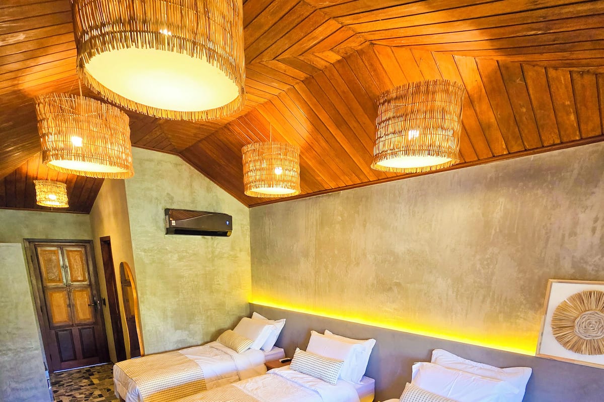 A hotel room with three beds, a patterned floor, wooden ceiling, and hanging lamps.