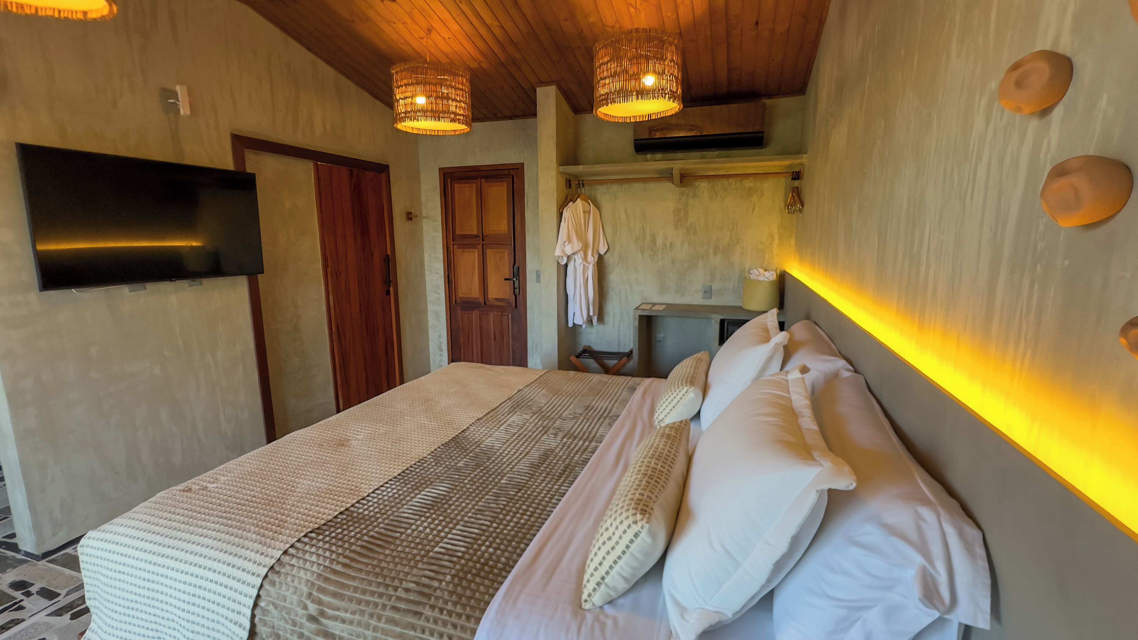 Een slaapkamer met een groot bed, houten plafond en een aan de muur bevestigde televisie.