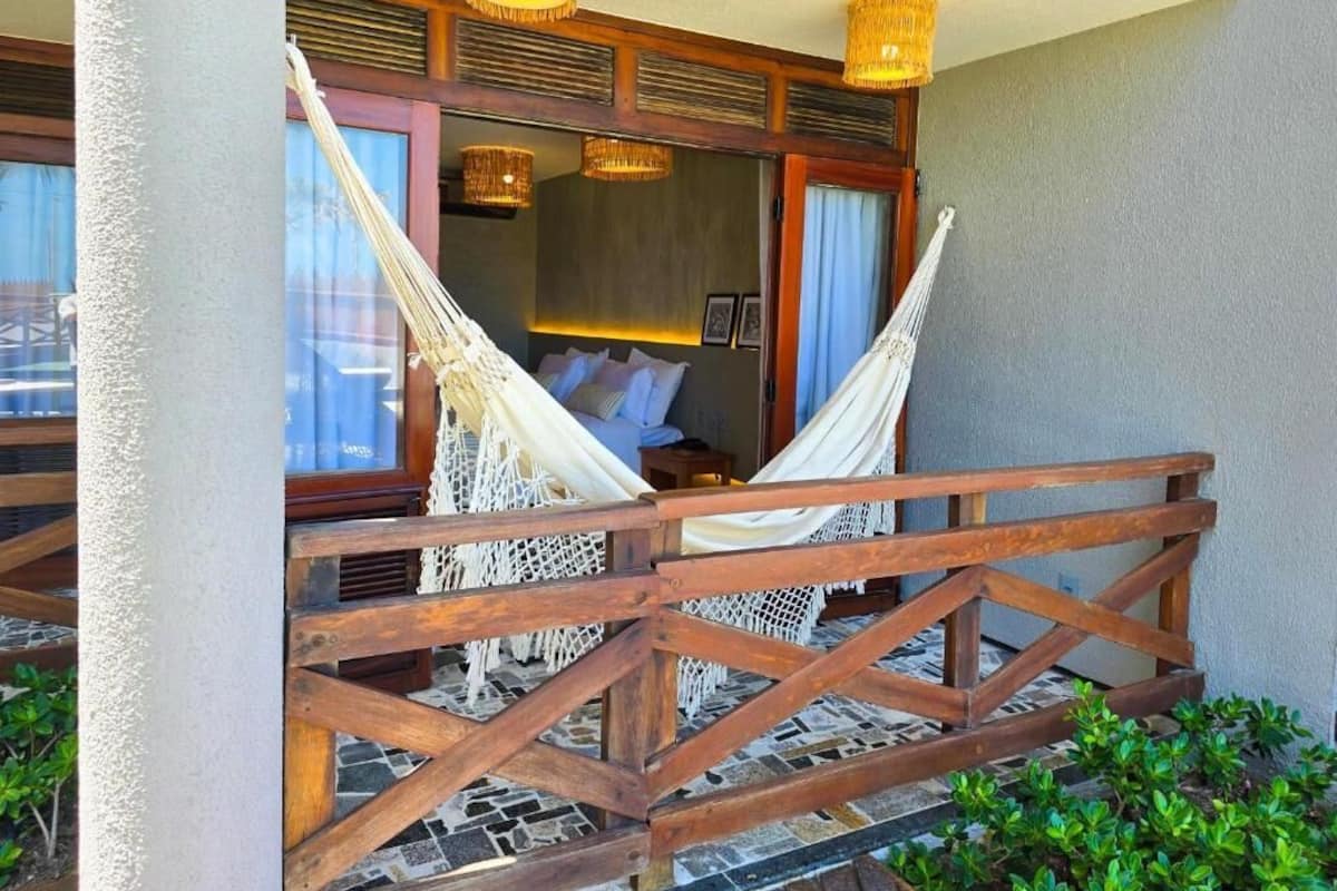 A hammock bed with a wooden railing, a window with curtains, and a wall-mounted light fixture.