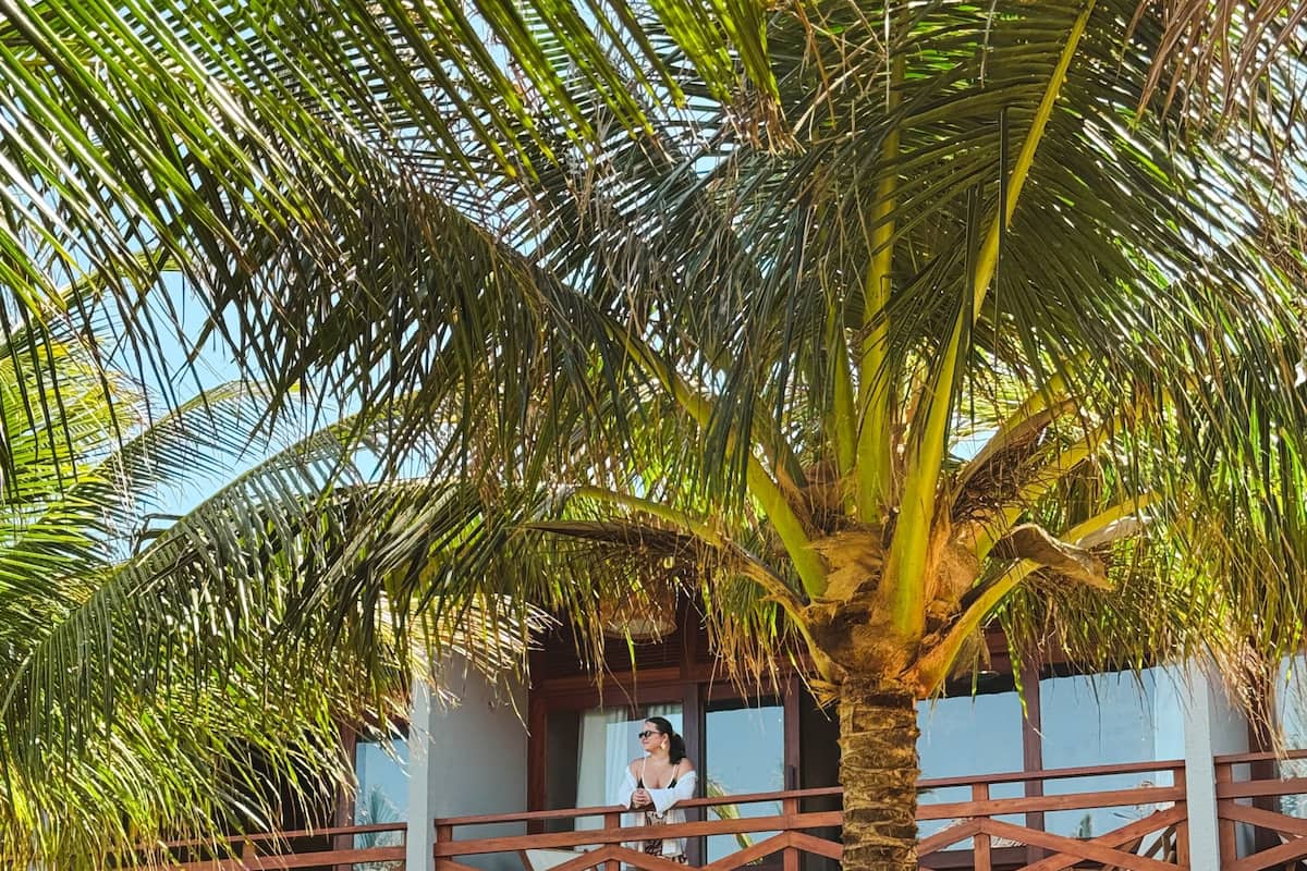 A resort with a covered outdoor seating area, palm trees, and a balcony overlooking the pool.