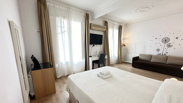A hotel room with a large bed, a desk, a sofa, and a TV. - Rooms Flor (Barcelona)