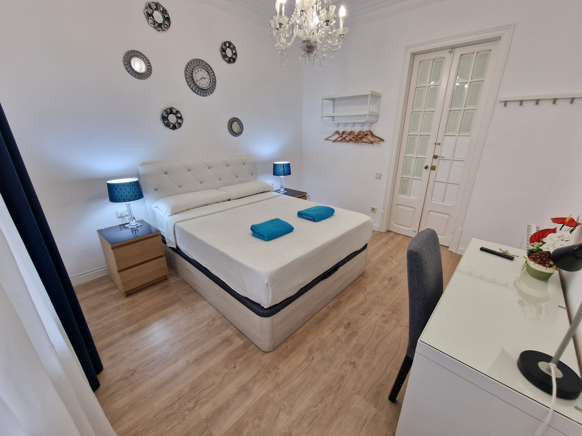 Un dormitorio con cama, mesitas de noche, escritorio, silla, candelabro y puerta.