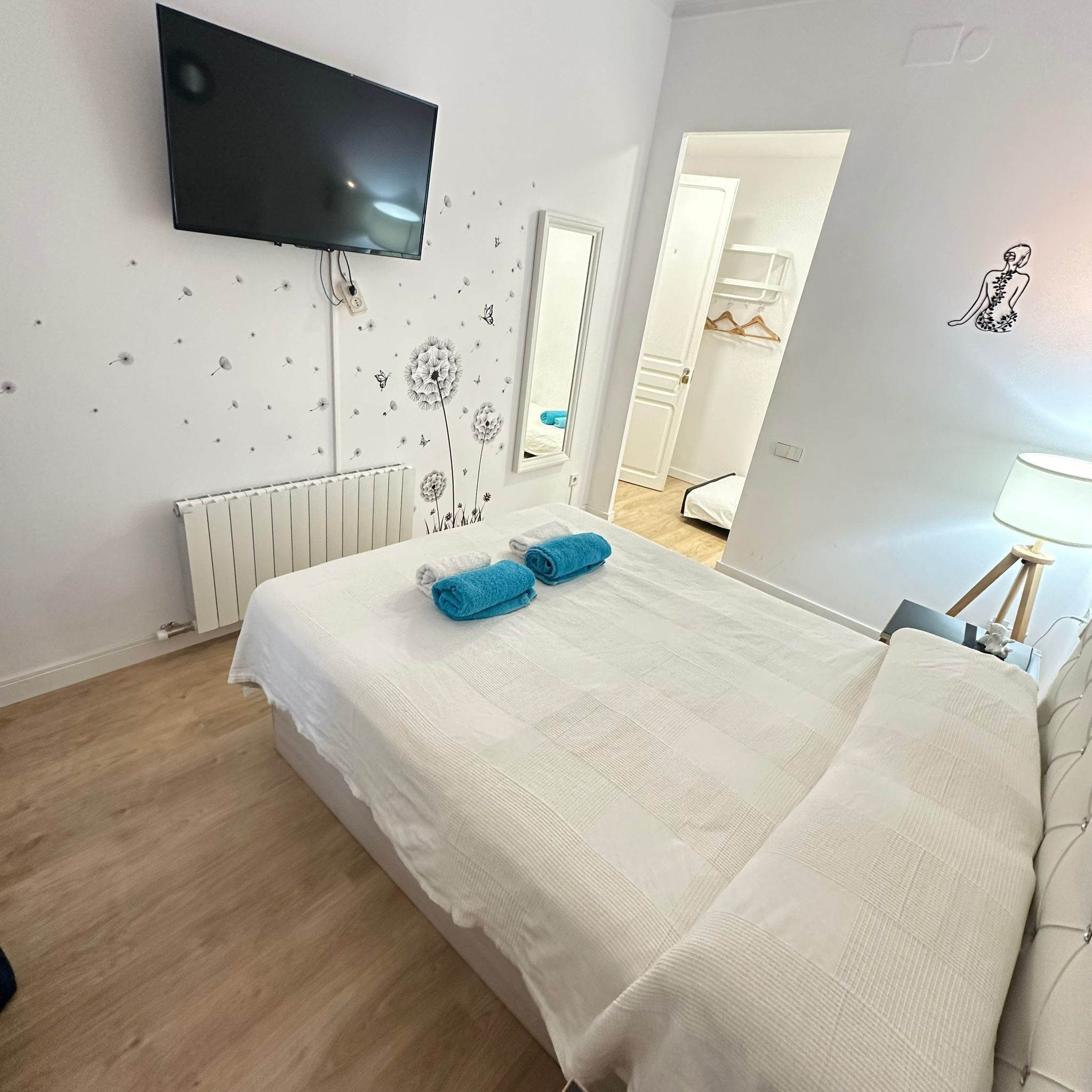 A bedroom with a bed, a TV mounted on the wall, a radiator, and a mirror.