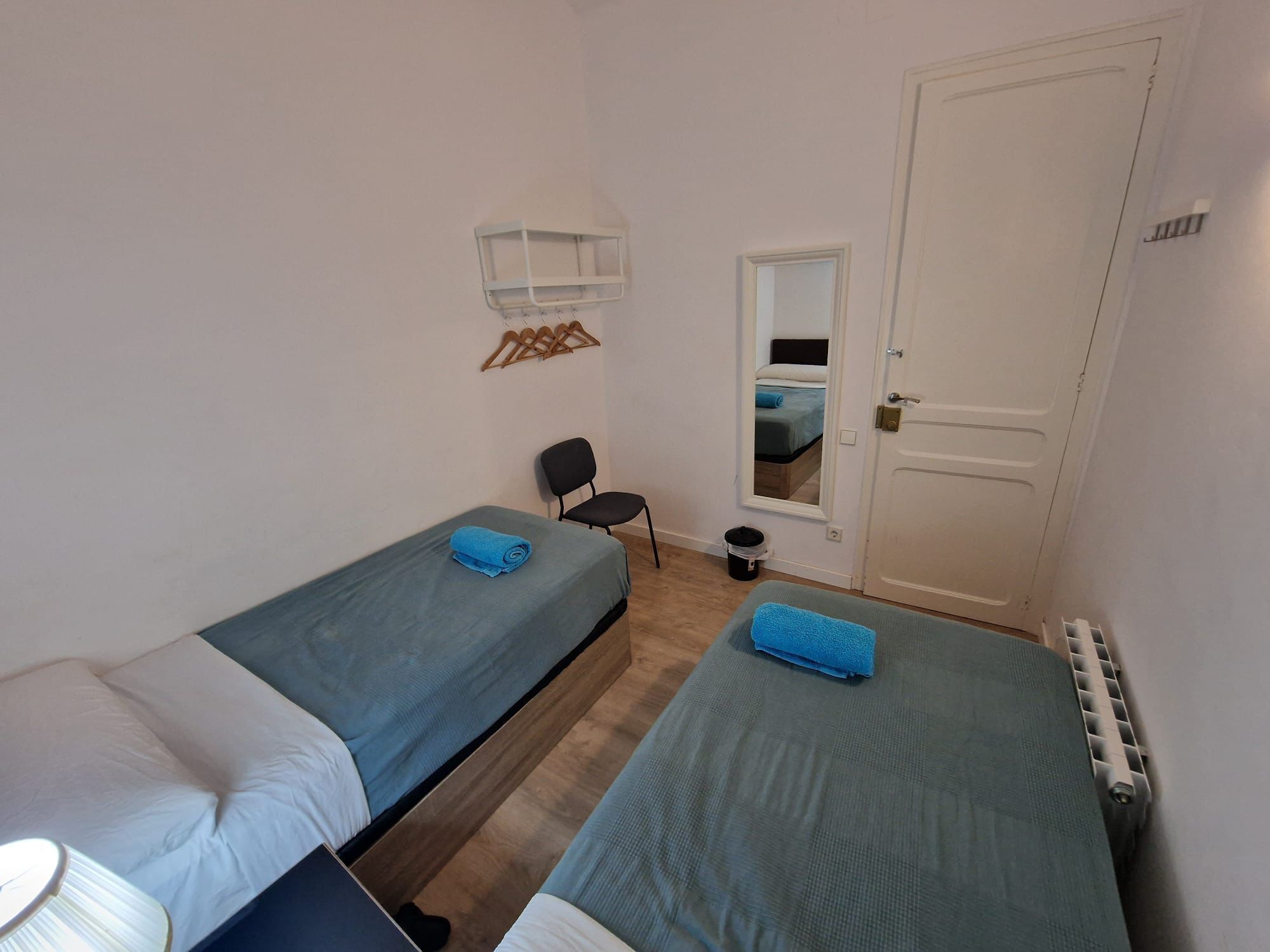 A small, clean room with two single beds, a chair, a mirror, and a radiator.