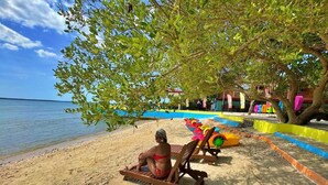 A beach with wooden lounge chairs and a pool area. - Arenzo Beach Resort Calatagan Batangas (Calatagan)