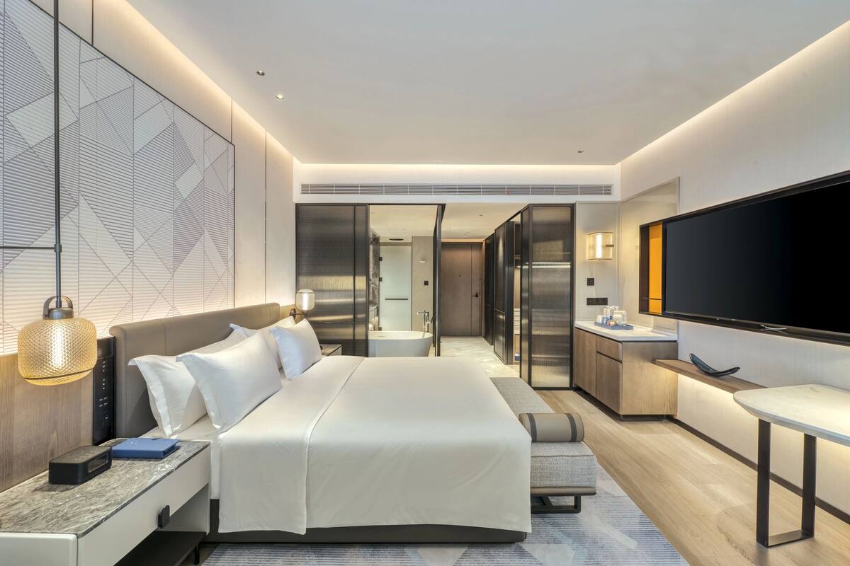 Une chambre d’hôtel moderne avec un grand lit, une table de chevet, une lampe et un téléviseur à écran plat.