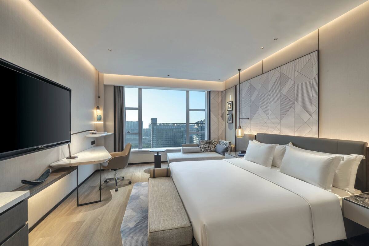 Une chambre d’hôtel moderne dotée d’un grand lit, d’une télévision à écran plat, d’un bureau et offrant une vue sur la ville.