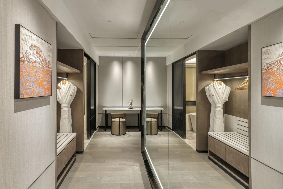A modern hotel corridor with mirrored walls, a central table, and seating areas.