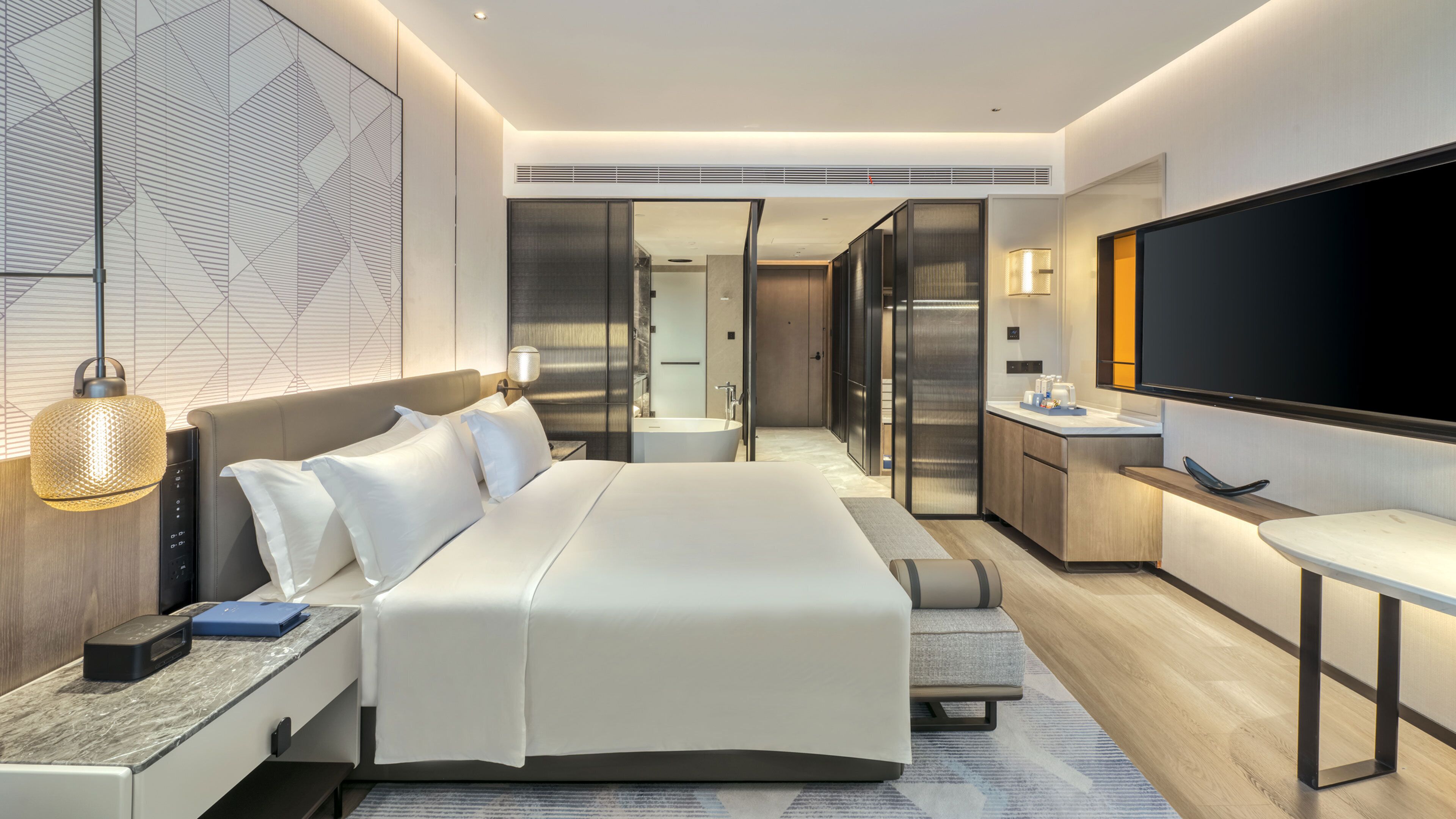 Une chambre d’hôtel moderne dotée d’un grand lit, d’un bureau, d’un téléviseur à écran plat et d’une salle de bain visible à travers une porte ouverte.
