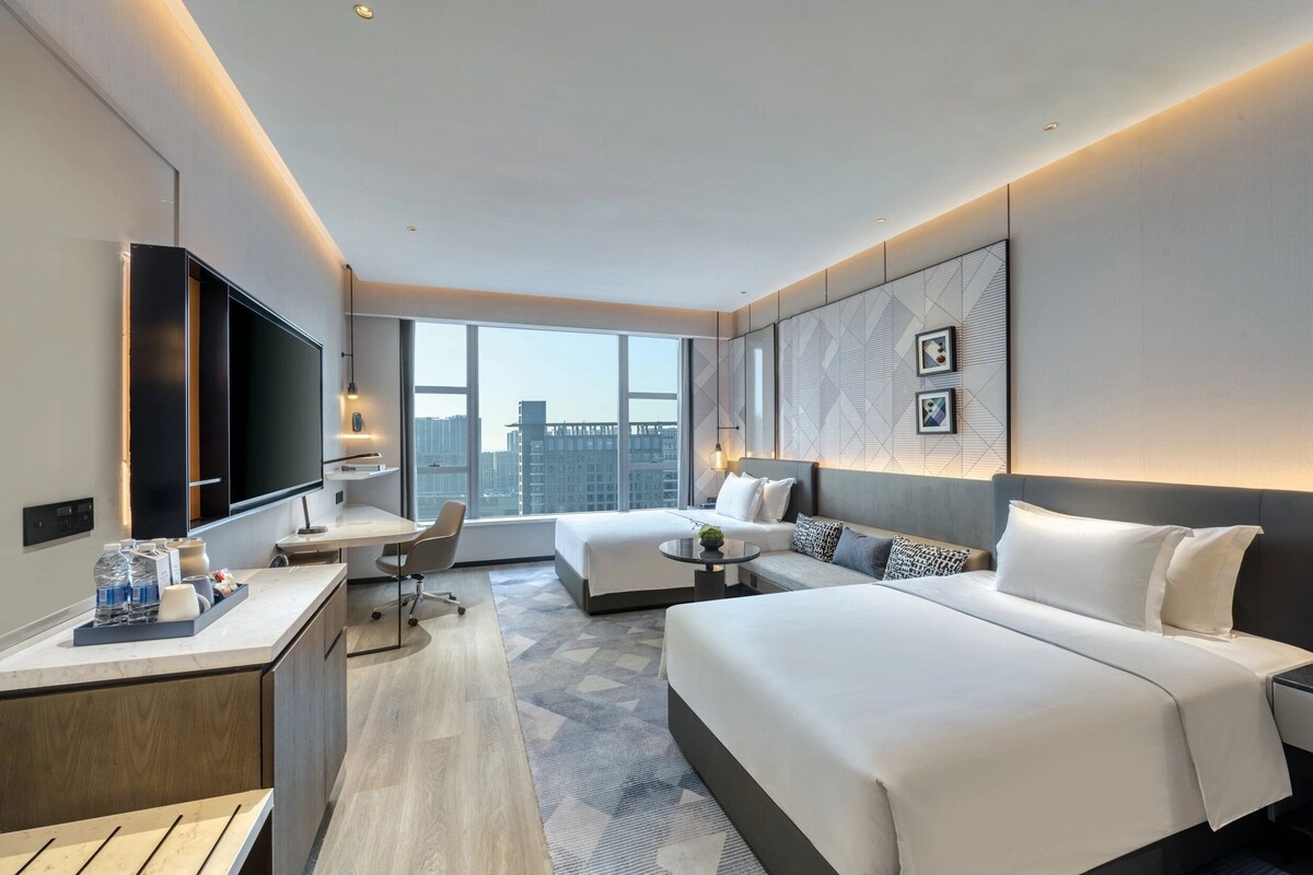 A modern hotel room with a large bed, a desk, a chair, and a TV.