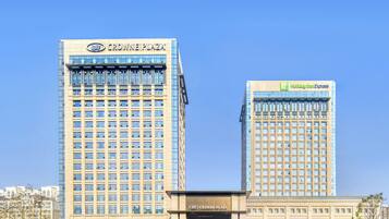 Two high-rise buildings with "Crowne Plaza" and "Holiday Inn Express" signage, surrounded by landscaped gardens and a clear sky.