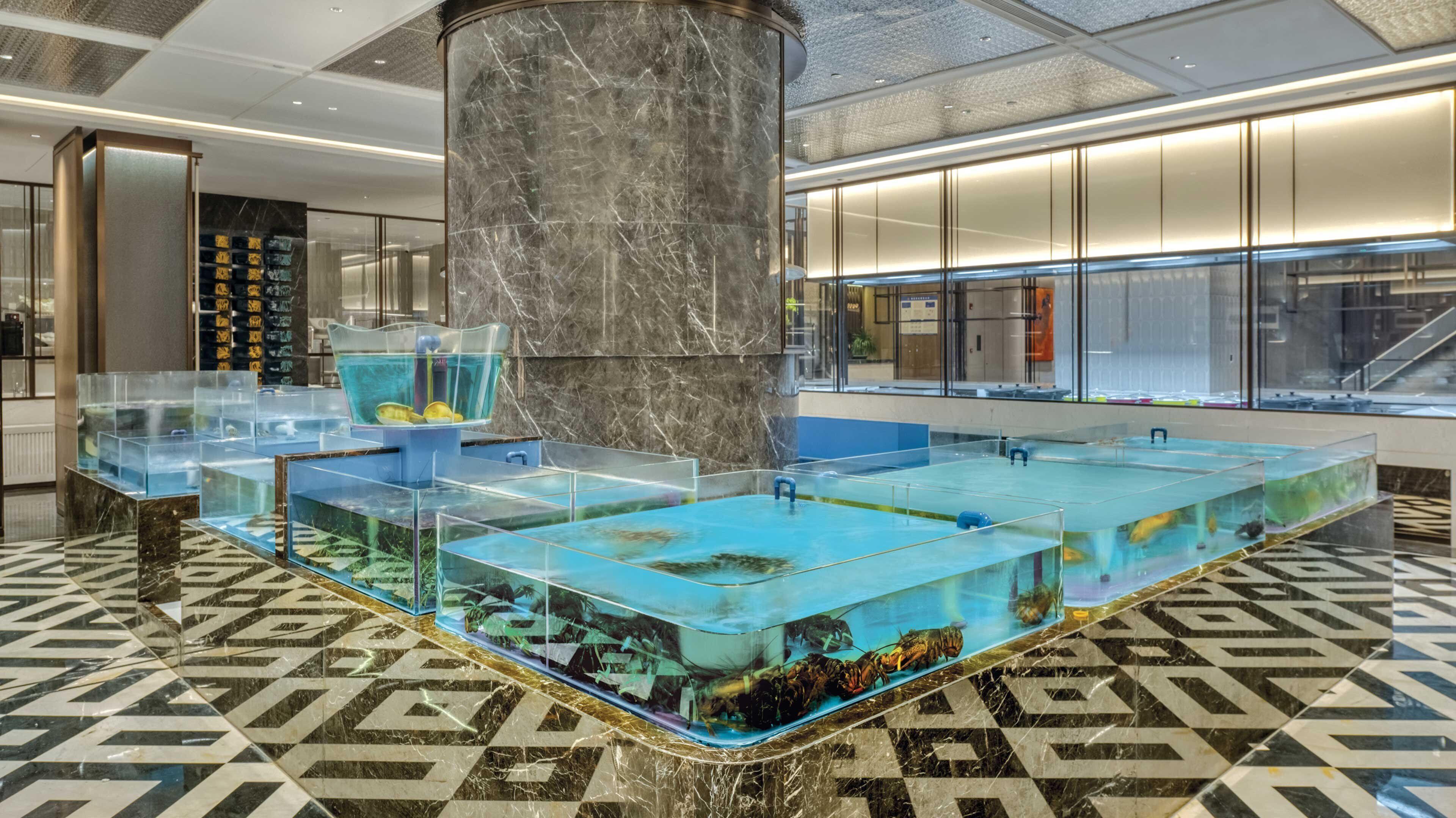 A modern lobby with a large marble column, multiple fish tanks, and a patterned floor.