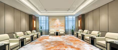 A conference room with a large, patterned carpet, beige sofas, and a central table with two chairs.