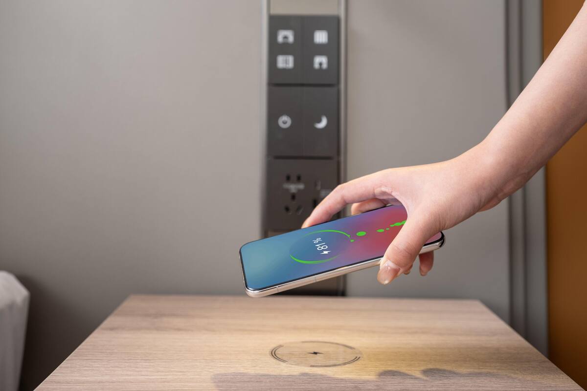 Eine Hand hält ein Smartphone mit einem farbenfrohen Bildschirm, das auf einem Holztisch mit einer kreisförmigen Vertiefung liegt.