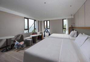 A modern hotel room with two beds, a small table, a chair, and a sofa.