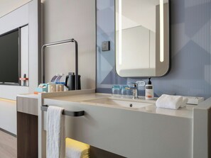 Un baño moderno con un espejo grande, un perchero para toallas, un lavamanos y una cafetera.
