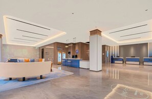 Un moderno vestíbulo de hotel con mostrador de recepción, zona de estar y una pantalla grande mostrando contenido.