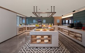 Cocina de hotel moderna con una isla central, diversos alimentos y una cafetera.