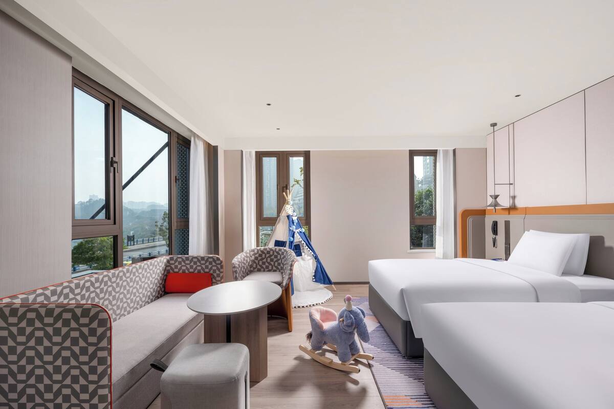 Una habitación de hotel moderna con un sofá, una mesita, una cama y un juguete de elefante mecedor.