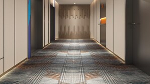Un pasillo moderno con alfombra estampada, iluminación empotrada y una franja de luz vertical en la pared.