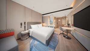 Una habitación de hotel moderna con una cama grande, un escritorio con una silla, un baño con espejo y una pantalla de televisión.