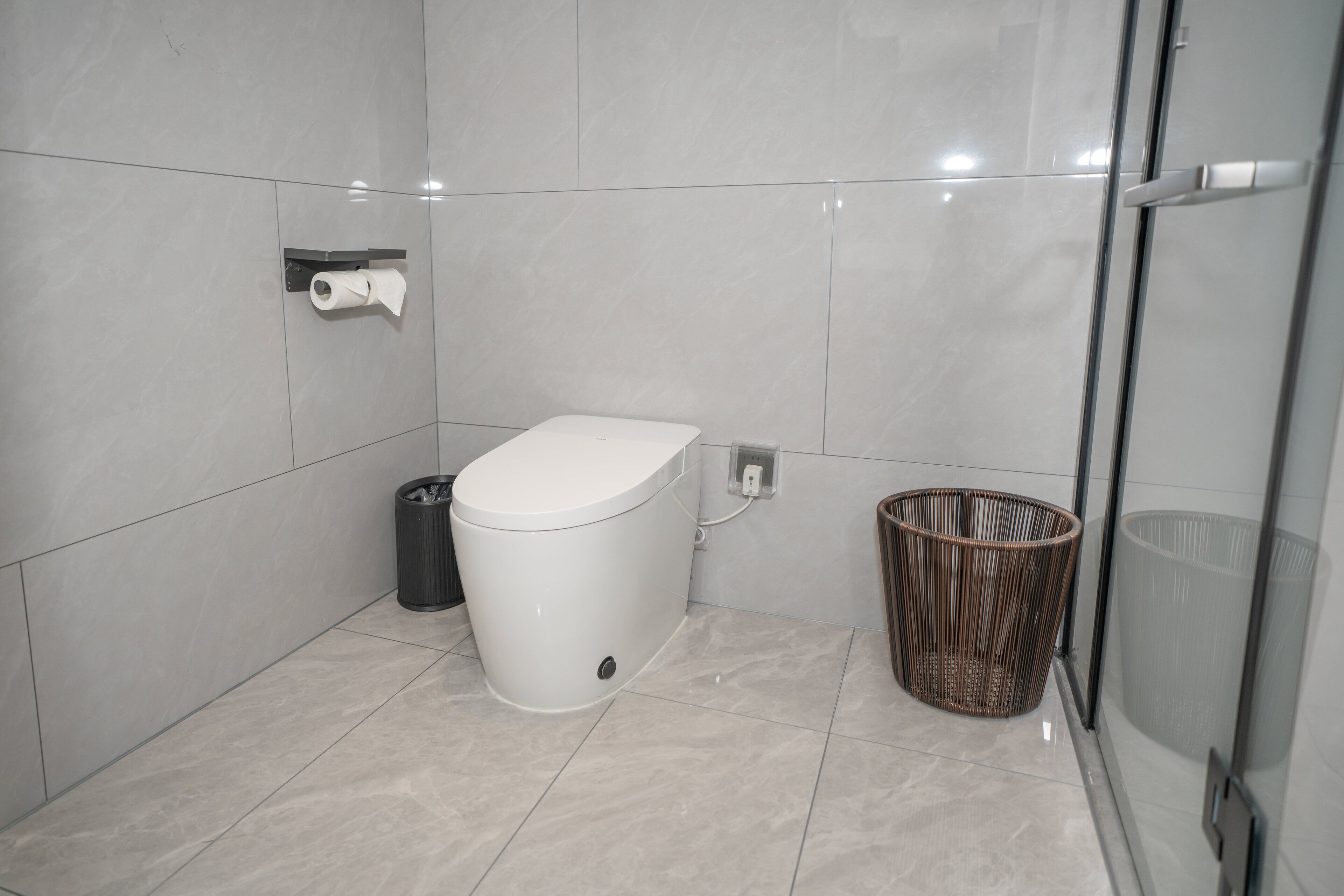 A modern bathroom with a toilet, a trash bin, and a wicker basket.