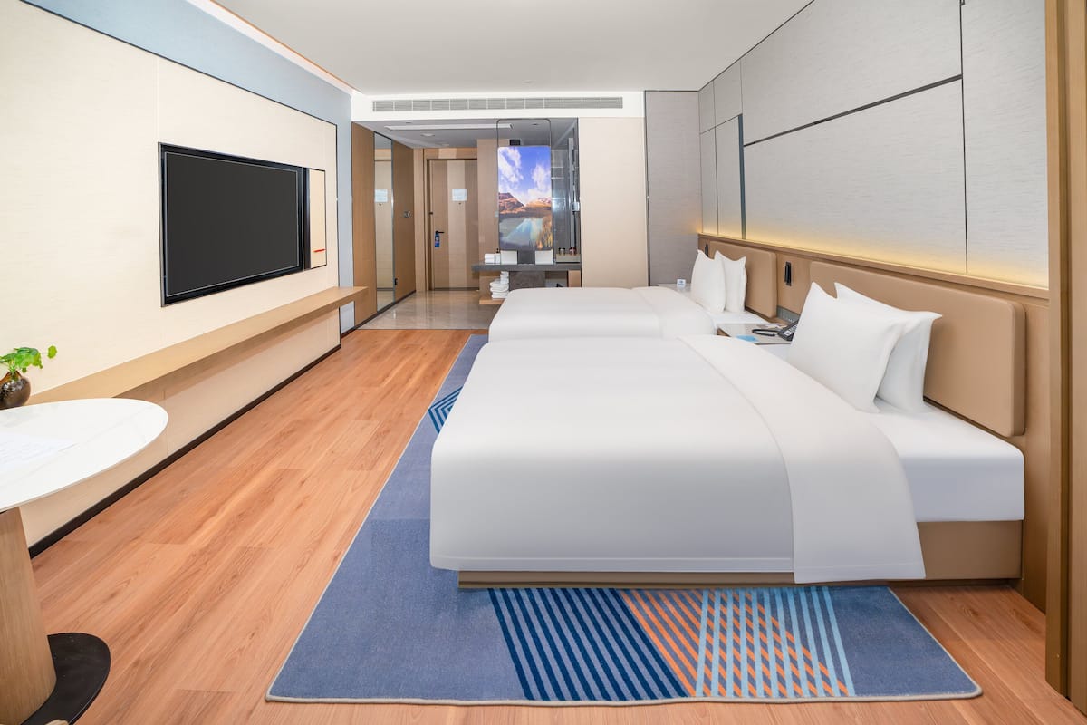 Habitación de hotel moderna con una cama grande, un televisor de pantalla plana, una mesita pequeña y vistas a la montaña desde la ventana.