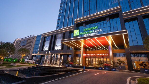 Un hotel Holiday Inn Express amb façana moderna, una fonteta al davant i indicadors en diverses llengües.