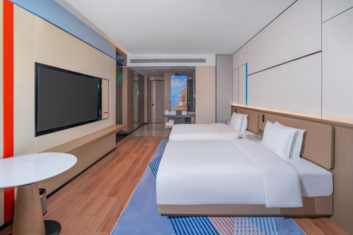 Een hotelkamer met een groot bed, een televisie, een klein tafeltje en uitzicht op een kustlandschap.