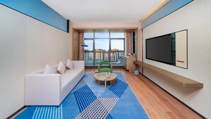 Habitació d'hotel moderna amb una finestra gran, un sofà, una taula de cafè i un televisor de pantalla plana.