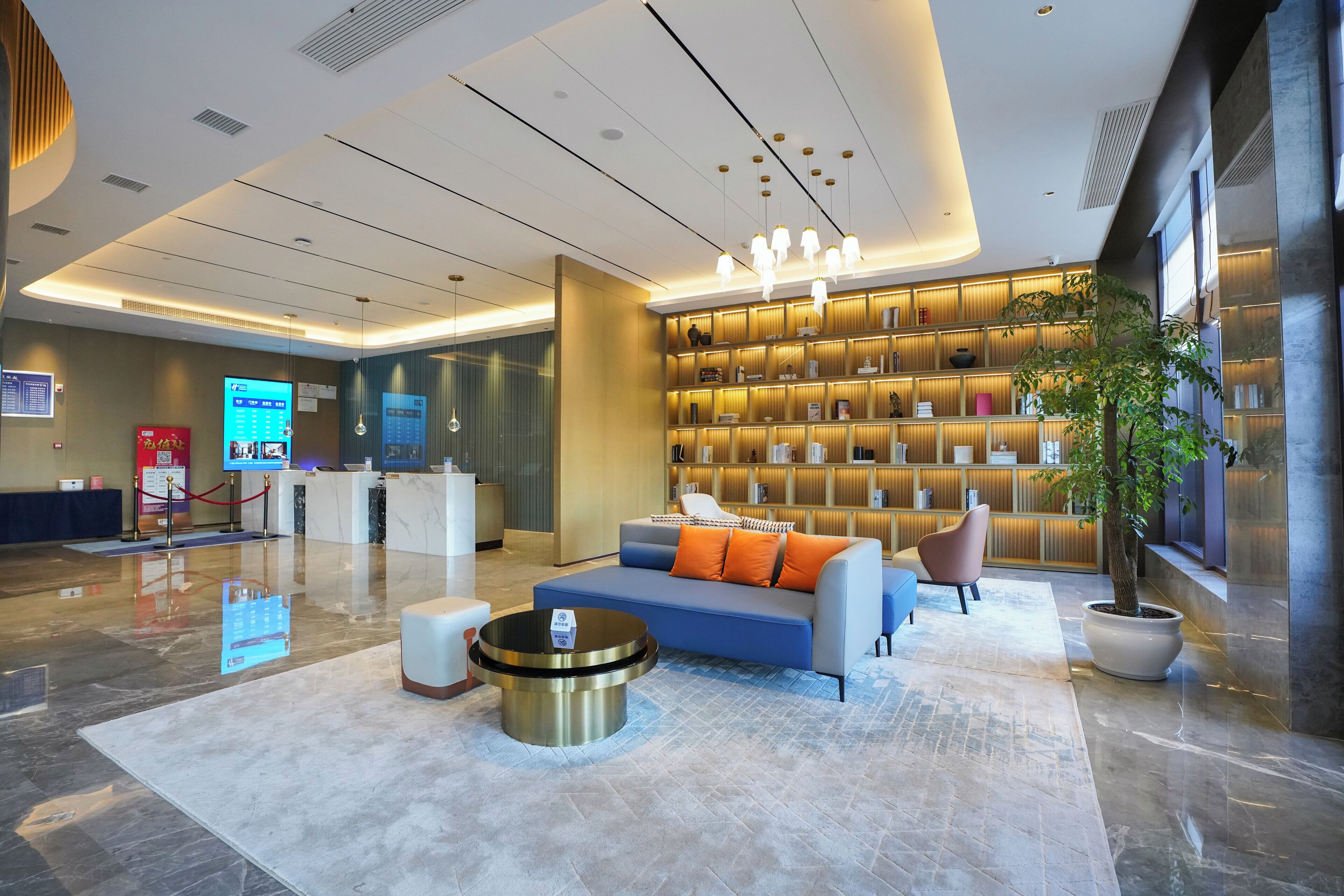 A modern lobby with a reception desk, seating area, and a large bookshelf.