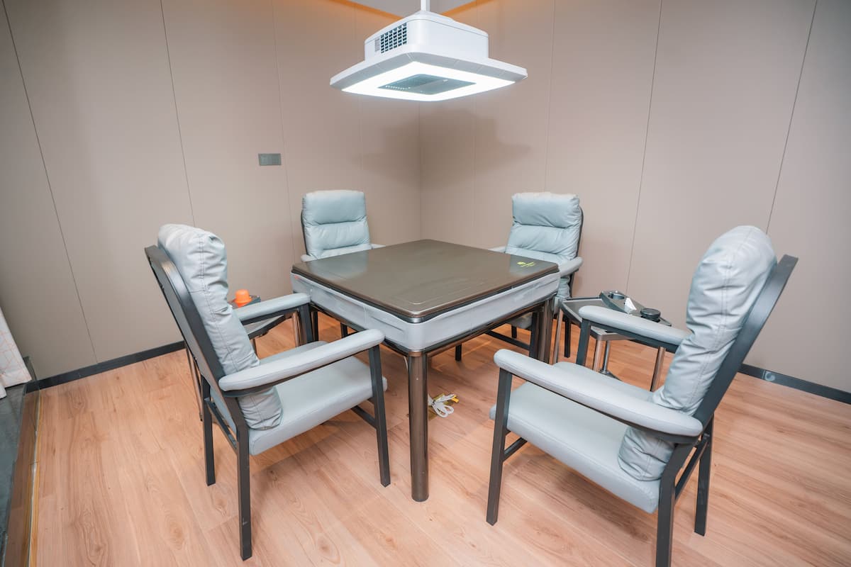 Un salón de conferencias con una mesa, cuatro sillas, un proyector y una pequeña mesa con una taza y una caja de pañuelos.