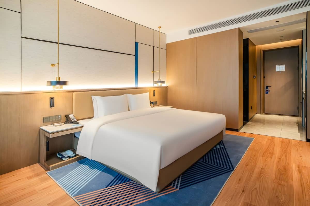 Una habitación de hotel moderna con una cama grande, una mesita de noche y un escritorio con teléfono.