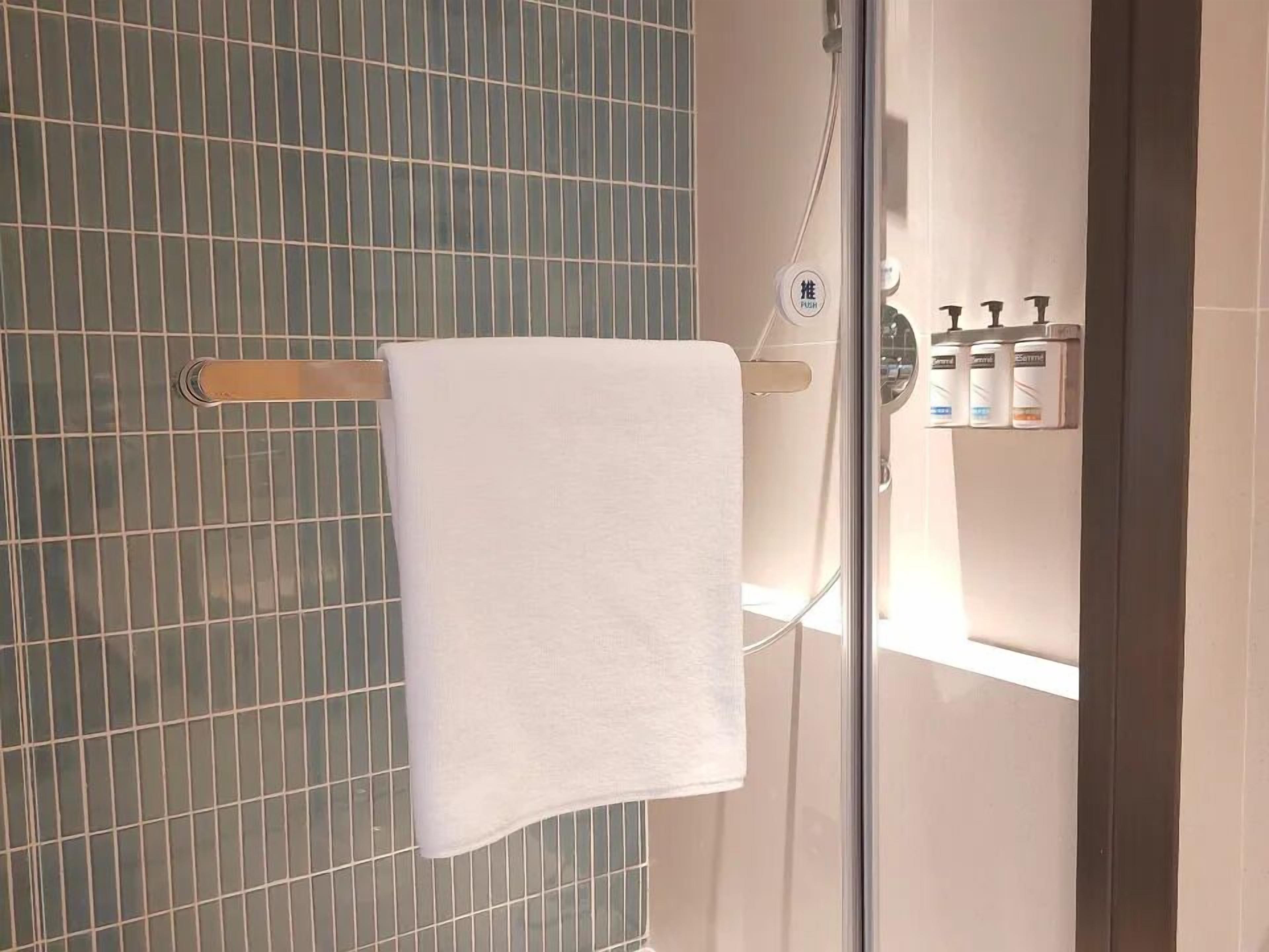 A bathroom with a towel hanging on a rack, a glass shower enclosure, and toiletries on a shelf.