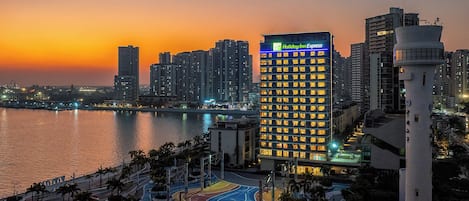 A Holiday Inn Express hotel with a waterfront view, surrounded by palm trees and a pedestrian bridge.