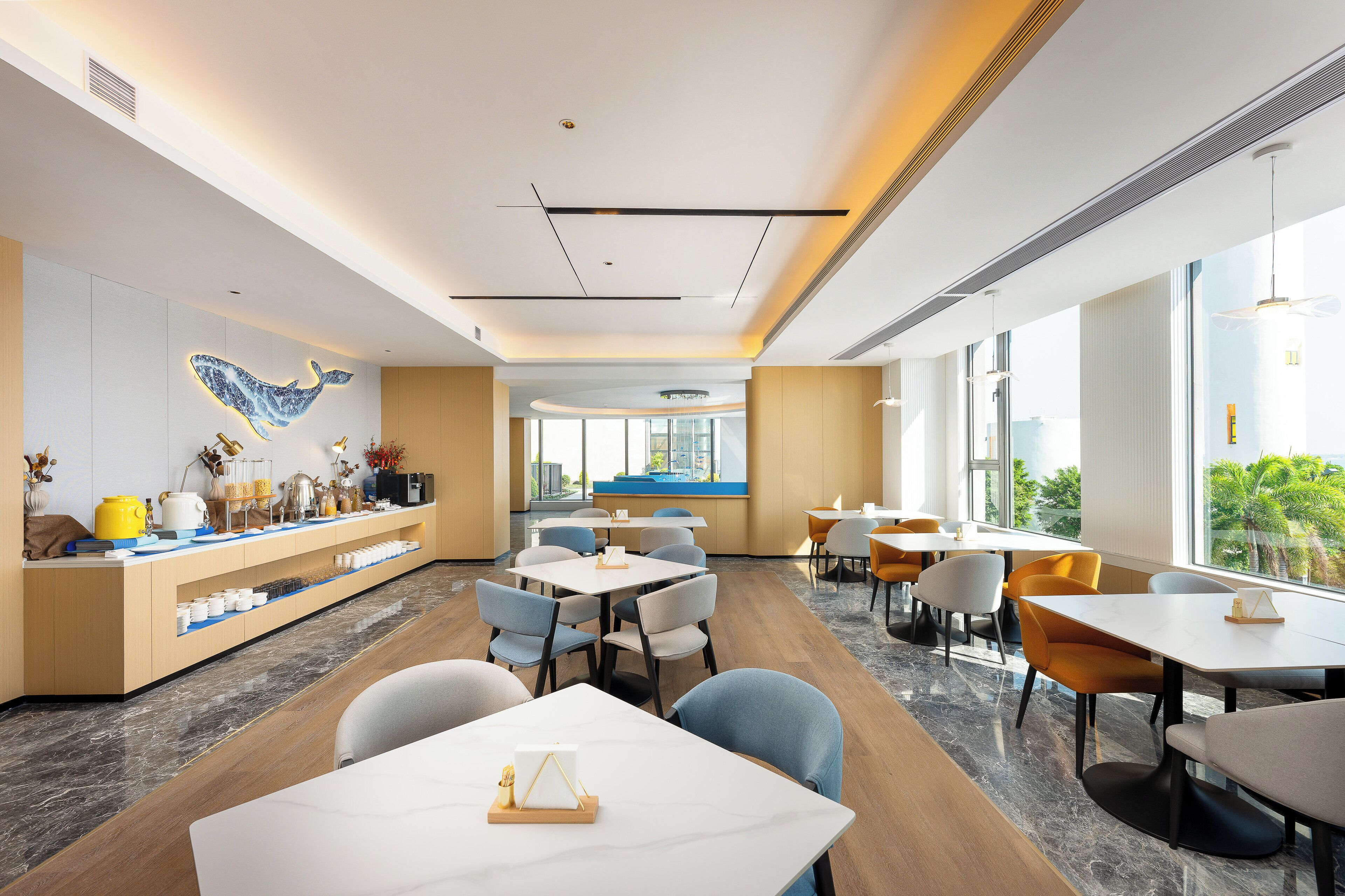 A modern dining area with a long counter, multiple tables, and chairs. There is a large window providing a view of the outdoors.